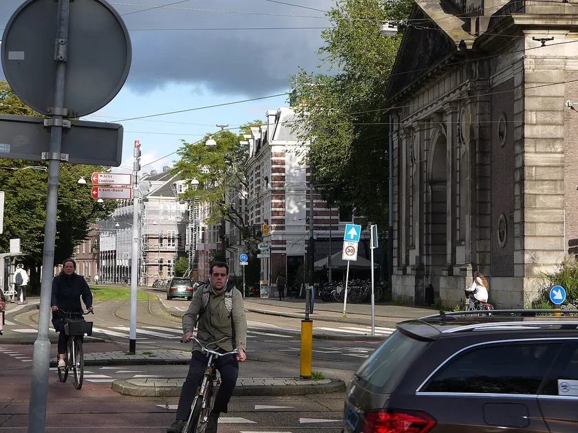 Cyclists on Sarphatistraat near the historic Muiderpoort gate illustrate how daily bike traffic reclaimed Amsterdam's urban streets.